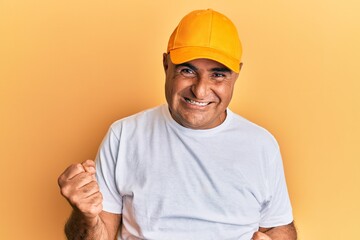 Mature middle east man with mustache wearing casual white tshirt and yellow cap celebrating surprised and amazed for success with arms raised and eyes closed