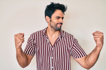 Handsome hispanic man with beard wearing casual clothes very happy and excited doing winner gesture with arms raised, smiling and screaming for success. celebration concept.