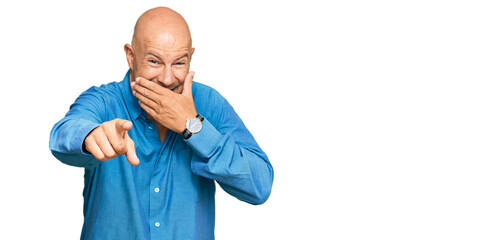 Middle age bald man wearing casual clothes laughing at you, pointing finger to the camera with hand over mouth, shame expression