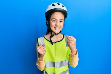 Beautiful brunette little girl wearing bike helmet and reflective vest excited for success with arms raised and eyes closed celebrating victory smiling. winner concept.