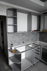 Custom kitchen cabinets installation without a furniture facades mdf. Gray modular kitchen from chipboard material on a various stages of installation in kitchen with a grey tile on floor and walls.