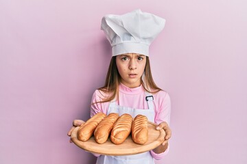 Beautiful brunette little girl wearing baker uniform holding homemade bread skeptic and nervous, frowning upset because of problem. negative person.