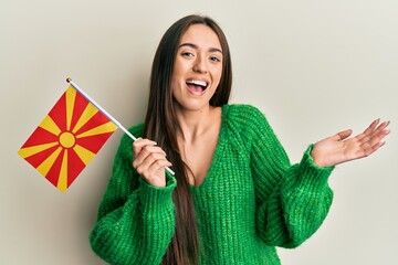 Young hispanic girl holding macedonian flag celebrating achievement with happy smile and winner expression with raised hand