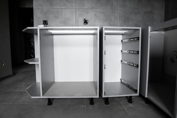 Custom kitchen cabinets installation without a furniture facades mdf. Gray modular kitchen from chipboard material on a various stages of installation in kitchen with a grey tile on floor and walls.