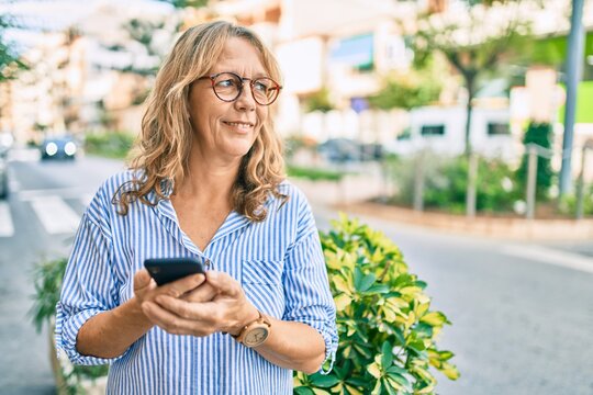 Middle age caucasian woman smiling happy using smartphone at the city.