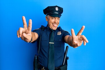 Handsome middle age mature man wearing police uniform smiling with tongue out showing fingers of both hands doing victory sign. number two.