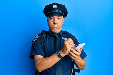 Handsome middle age mature man wearing police uniform writing a ticket puffing cheeks with funny face. mouth inflated with air, catching air.