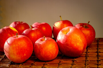 Several ripe red apples stand on a wicker basket illuminated by rays of the sun