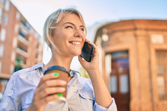 Young blonde woman smiling happy talking on the smartphone and drinking take away coffee at the city.