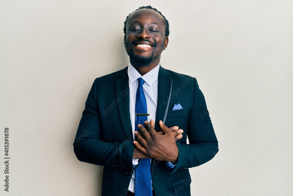 Sticker handsome young black man wearing business suit and tie smiling with hands on chest with closed eyes 