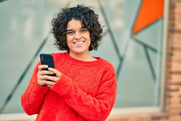 Young hispanic woman smiling happy using smartphone at the city