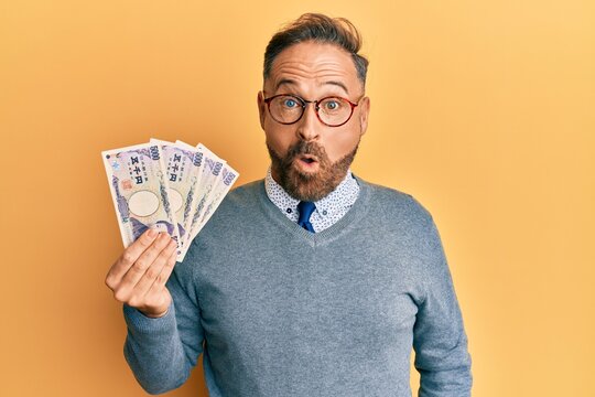 Handsome middle age man holding 5000 japanese yen banknotes scared and amazed with open mouth for surprise, disbelief face