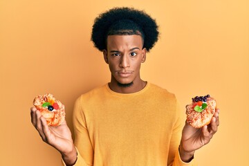 African american man with afro hair holding sweet pastries skeptic and nervous, frowning upset...