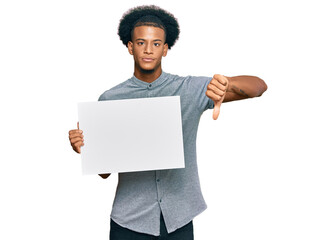 African american man with afro hair holding blank empty banner with angry face, negative sign...