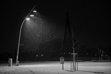 Snow flurries on a square in the evening, street lights and snow flurries, it snows in the evening on a large, illuminated square, black and white photo