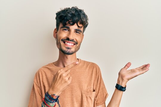 Young hispanic man wearing casual clothes amazed and smiling to the camera while presenting with hand and pointing with finger.