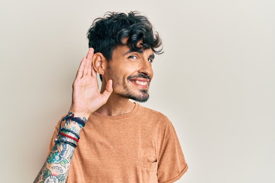 Young hispanic man wearing casual clothes smiling with hand over ear listening an hearing to rumor or gossip. deafness concept.