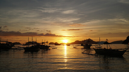 Sunset over the ocean with boats at El Nido Beach in Philippines.