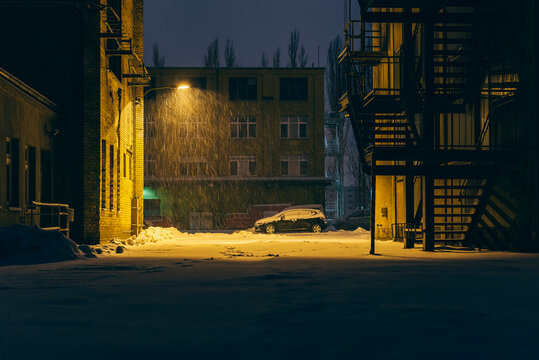 A parking lot in an industrial setting in the evening and when it is snowing, street lights, snowfall, parking lot