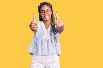 Young african american woman with braids wearing casual summer clothes and glasses approving doing positive gesture with hand, thumbs up smiling and happy for success. winner gesture.