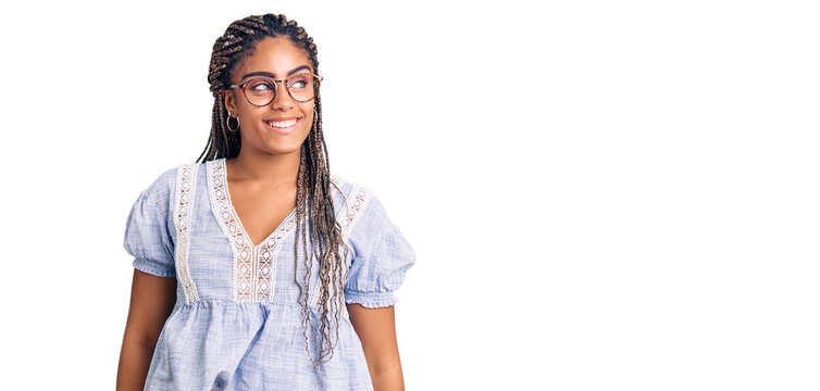 Young african american woman with braids wearing casual summer clothes and glasses looking away to side with smile on face, natural expression. laughing confident.