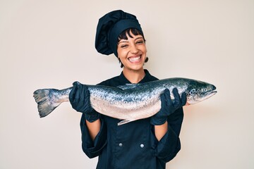 Beautiful brunettte woman professional chef holding fresh salmon fish smiling with a happy and cool...