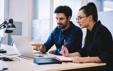 Smiling colleagues preparing report together working on laptop
