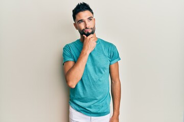 Young man with beard wearing casual clothes thinking concentrated about doubt with finger on chin and looking up wondering