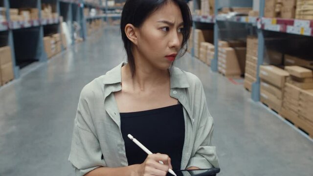 Unhappy young Asia businesswoman looking and feeling confused using digital tablet checking inventory levels standing in retail shopping center. Distribution, Logistics, Packages ready for shipment.