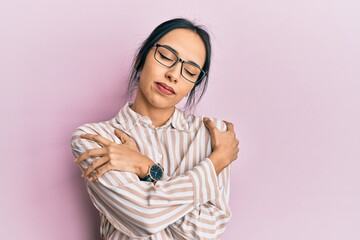 Young hispanic girl wearing casual clothes and glasses hugging oneself happy and positive, smiling...