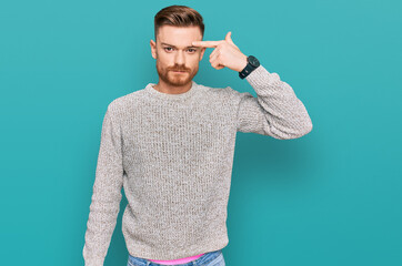 Young redhead man wearing casual winter sweater pointing unhappy to pimple on forehead, ugly...