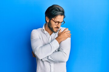 Young hispanic man wearing casual clothes and glasses hugging oneself happy and positive, smiling...