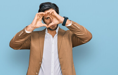 Young hispanic man wearing business clothes doing heart shape with hand and fingers smiling looking through sign