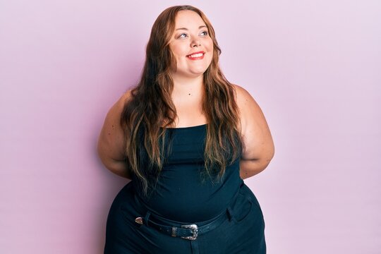 Plus size caucasian young woman wearing casual clothes over pink background looking to side, relax profile pose with natural face and confident smile.