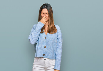 Young woman wearing casual clothes smelling something stinky and disgusting, intolerable smell, holding breath with fingers on nose. bad smell - obrazy, fototapety, plakaty