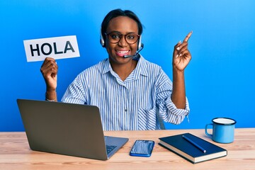 Young african woman wearing operator headset holding hola word smiling happy pointing with hand and finger to the side © Krakenimages.com