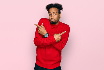 Young african american man with beard wearing casual winter sweater pointing to both sides with fingers, different direction disagree