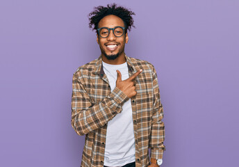 Young african american man with beard wearing casual clothes and glasses cheerful with a smile on face pointing with hand and finger up to the side with happy and natural expression