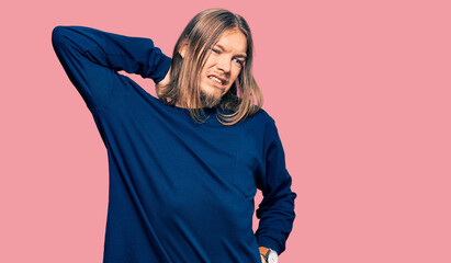 Handsome caucasian man with long hair wearing casual winter sweater suffering of neck ache injury, touching neck with hand, muscular pain