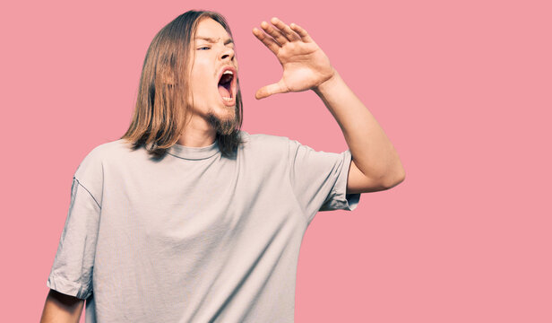 Handsome caucasian man with long hair wearing casual clothes shouting and screaming loud to side with hand on mouth. communication concept.