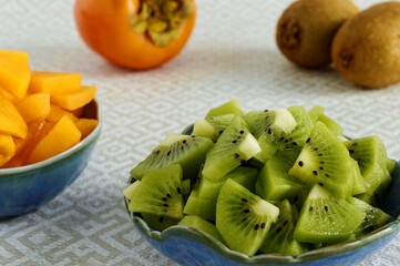 Persimmon and kiwifruit pieces in small bowls. Copped row fruits snack salad.