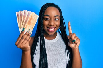 Young african american woman holding 500 norwegian krone banknotes smiling with an idea or question...