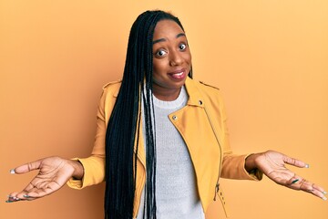 Young african american woman wearing casual jacket clueless and confused expression with arms and...