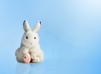 Easter bunny rabbit with pink painted egg on blue background. Easter holiday concept.
