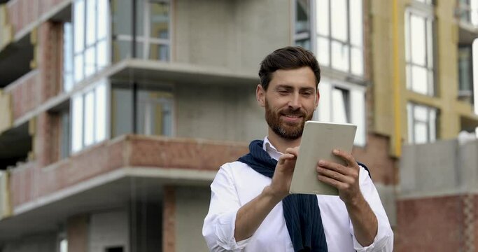 Handsome bearded man in blue sweater sitting outdoors and using portable laptop. Smiling male working on wireless computer on fresh air.