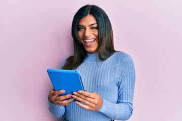 Young latin transsexual transgender woman using touchpad device winking looking at the camera with...