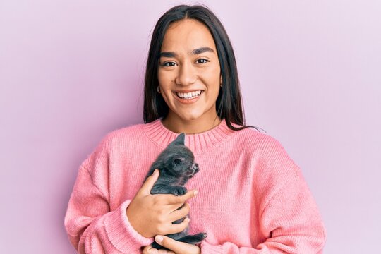 Young hispanic girl smiling happy holding cute cat over isolated pink background.