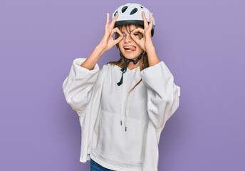 Teenager caucasian girl wearing bike helmet doing ok gesture like binoculars sticking tongue out, eyes looking through fingers. crazy expression.