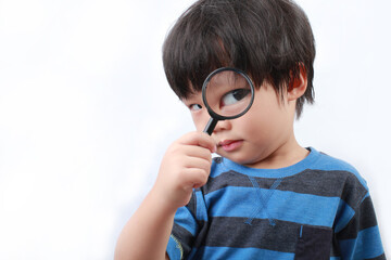 Portrait of Asian boy using a magnifying glass. Cute little boy look through the magnifying glass and his eye is enlarged.
