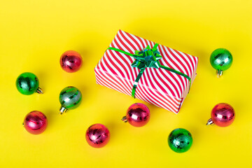 Christmas card with gift box and shiny balls on a yellow background. Colorful New Year background, festive decorations.
